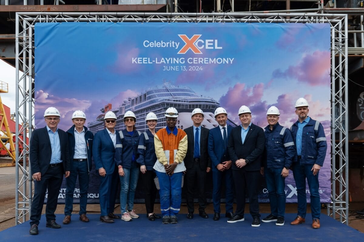 A group of people in hard hats and business attire stand in front of a banner that reads