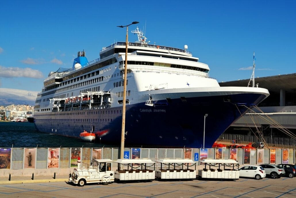 Large cruise ship docked at a port with cars and generator trailers parked nearby under a clear blue sky, ready for its year-round sailings.