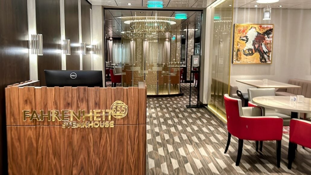 Elegant interior of the Carnival Mardi Gras Fahrenheit 555 steakhouse with reception desk and dining area.