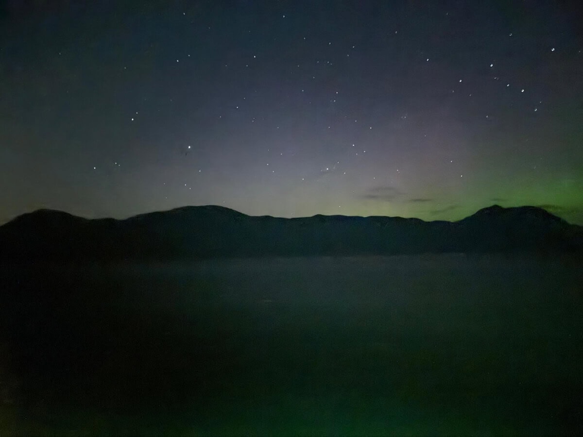 Nighttime landscape showing a faint aurora over dark silhouetted mountains during an Alaska Trip under a starry sky.