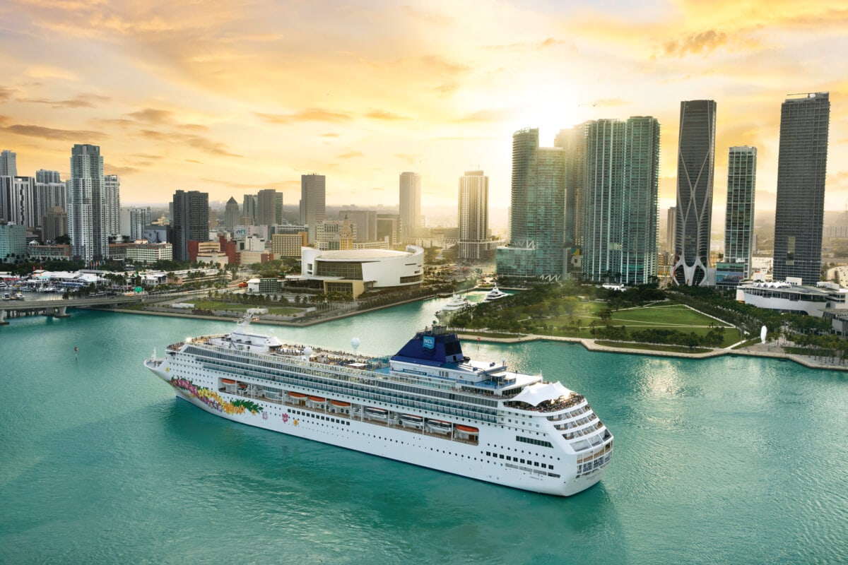 Cruise ship departing from a modern city's port at sunset, heading towards the British Virgin Islands.